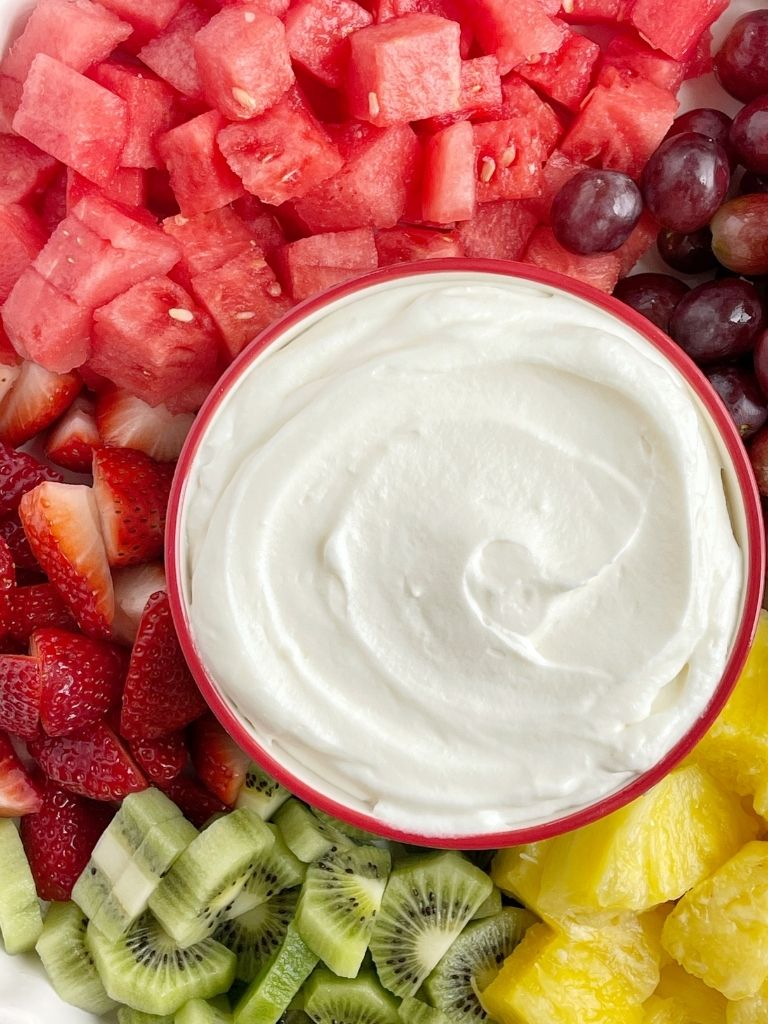 Fruit dip recipe with coconut cream and freshly whipped cream on a plate with fresh cut fruit. 