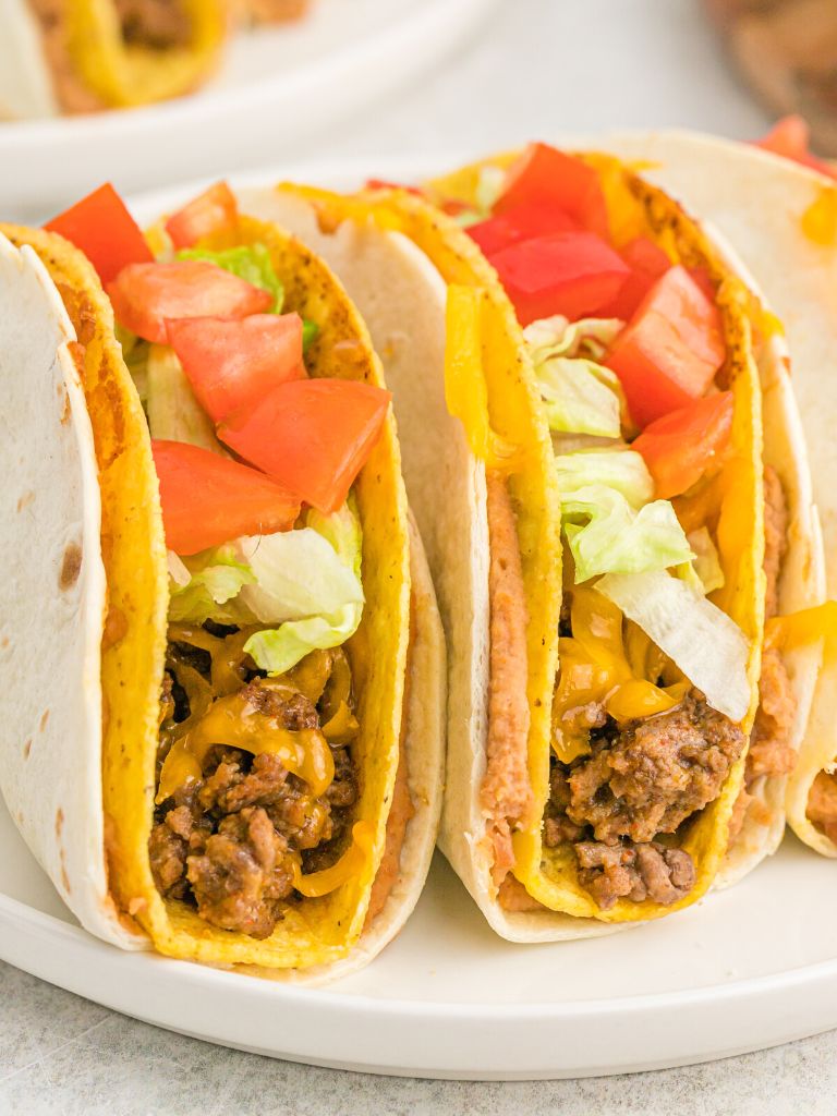 Side shot of double decker tacos on a white plate.