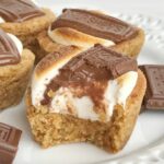 S'mores cookie cups are baked in a mini muffin pan. Graham cracker cookie base, with a toasted marshmallow, and a piece of gooey chocolate on top! Now you can enjoy campfire toasty s'more all year round for dessert.