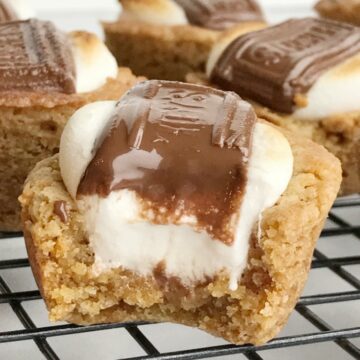 S'mores cookie cups are baked in a mini muffin pan. Graham cracker cookie base, with a toasted marshmallow, and a piece of gooey chocolate on top! Now you can enjoy campfire toasty s'more all year round for dessert.