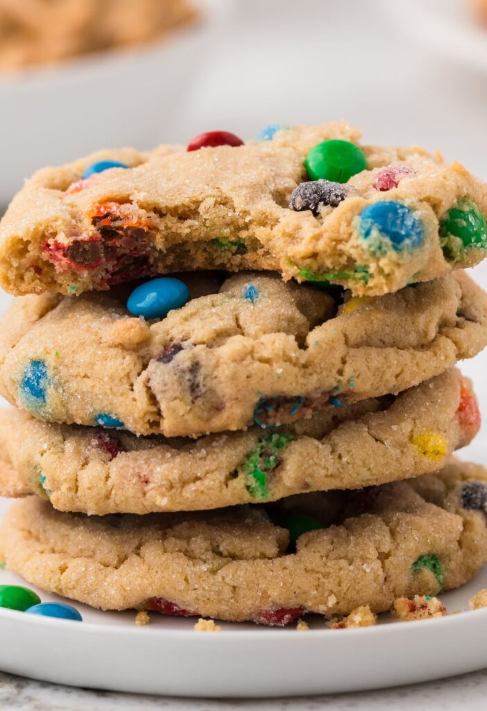 Stack of peanut butter cookies with m&m's in them, the top cookie has a bite taken out of it. 