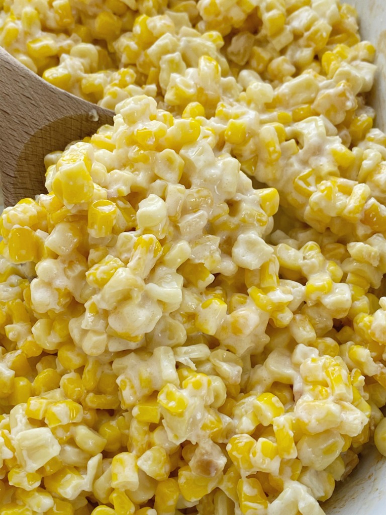 A close up picture of slow cooker creamed corn with a wooden spoon. 