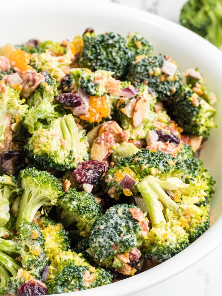 A white bowl with broccoli salad inside of it. 