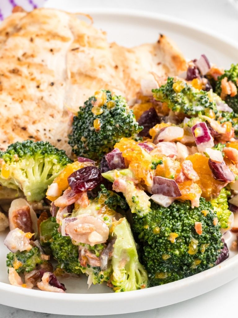 Broccoli salad with bacon, oranges, and almonds on a white plate with some chicken. 
