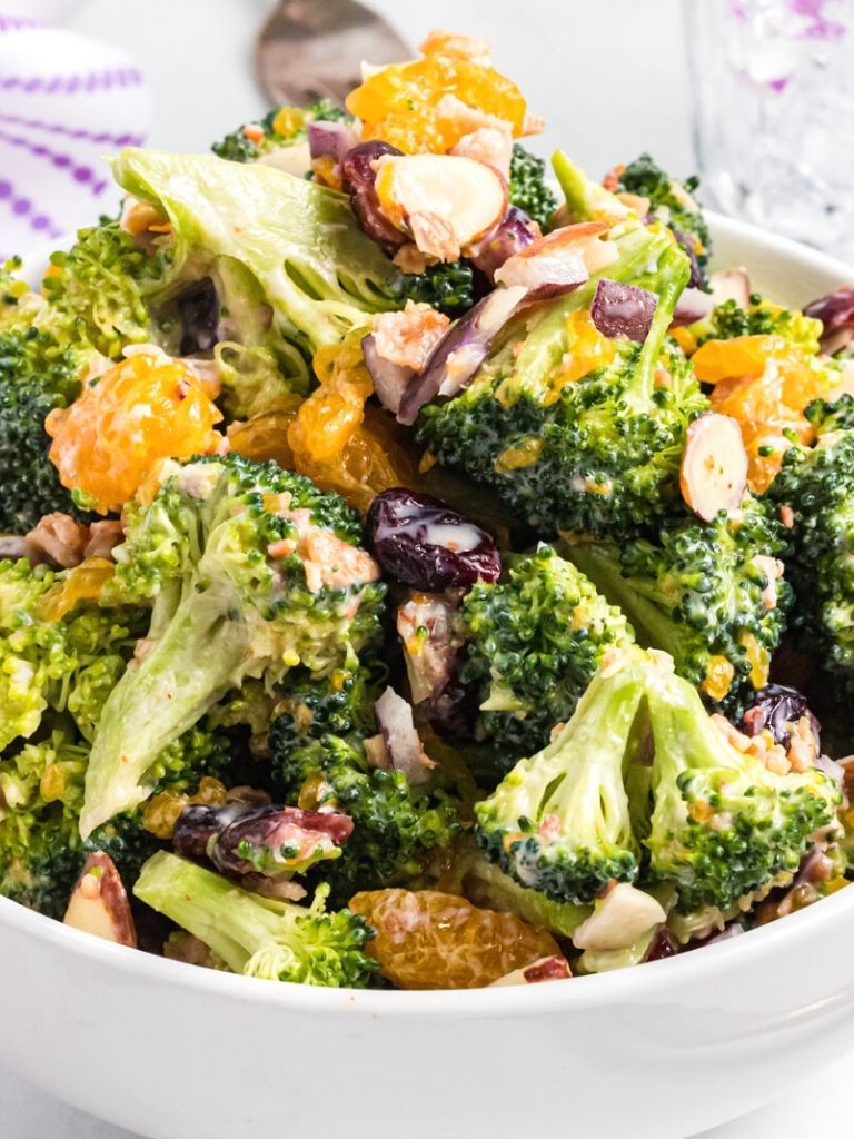 broccoli salad inside a white bowl with a fork holding some up to show the texture. 