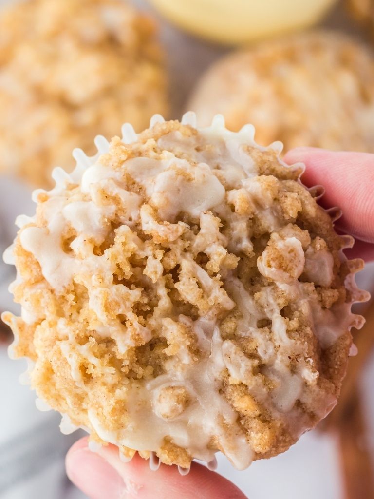 A hand holding a muffin that shows a close up of the crumble topping and glaze. 