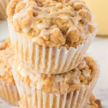A stack of muffins on top of each other topped with a crumble topping and eggnog glaze.
