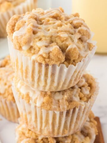 A stack of muffins on top of each other topped with a crumble topping and eggnog glaze.