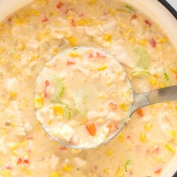 A white pot with chicken corn chowder inside of it and a soup ladle with some in it.