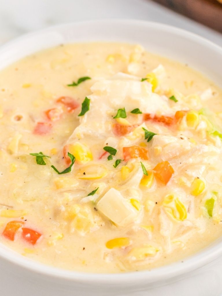 A white bowl with chowder inside of it with chicken and corn. 