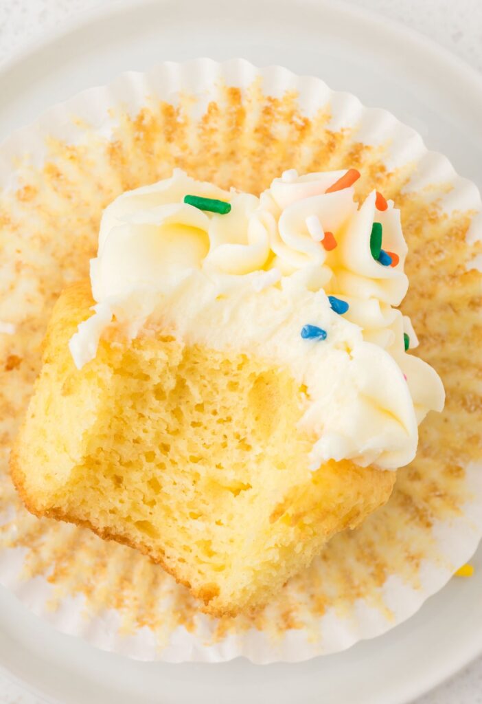 A cupcake with a bite out of it, laying on its side on a cupcake wrapper.