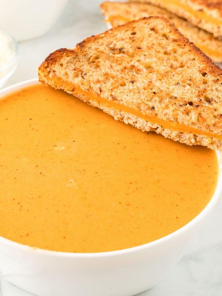 A bowl of tomato soup with a grilled cheese sandwich on the side of the bowl.