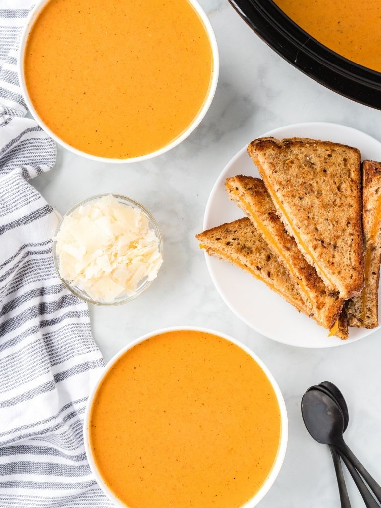 Tomato soup inside 3 bowls on the counter with grilled cheese on the side. 