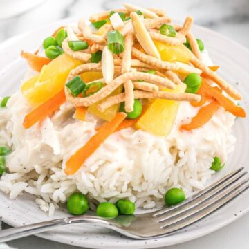 Plate with rice, chicken gravy, and topped with chow mien, cheese, peas, and pineapple.