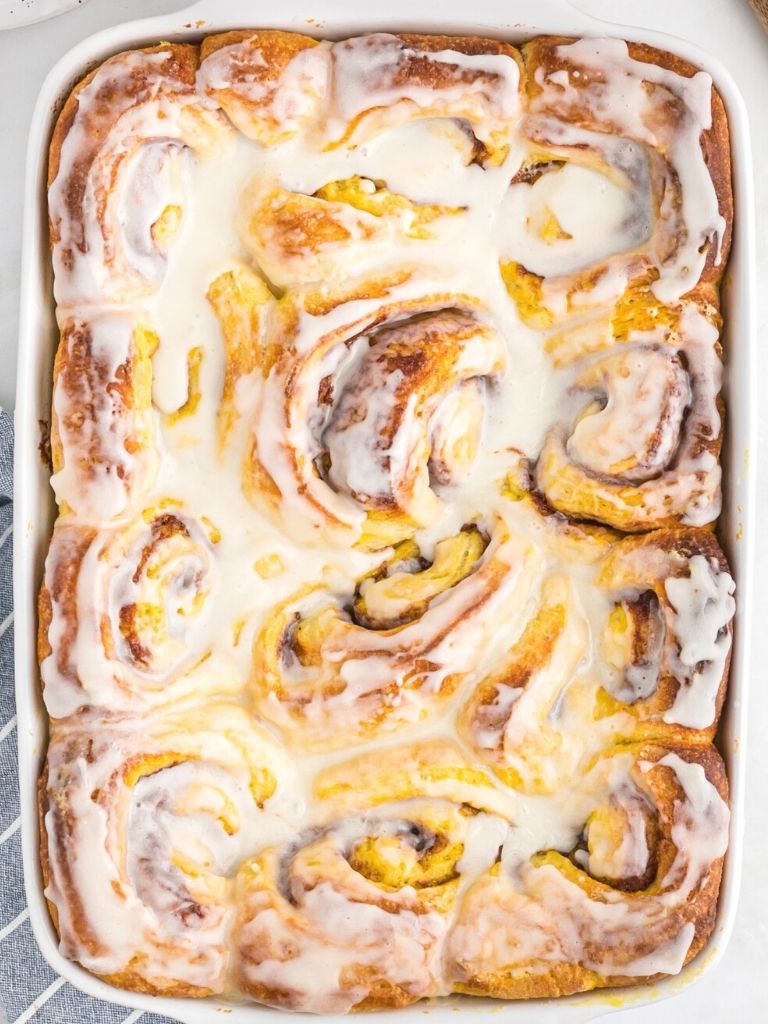 Vertical picture of a white pan with frosted cinnamon rolls inside of it.
