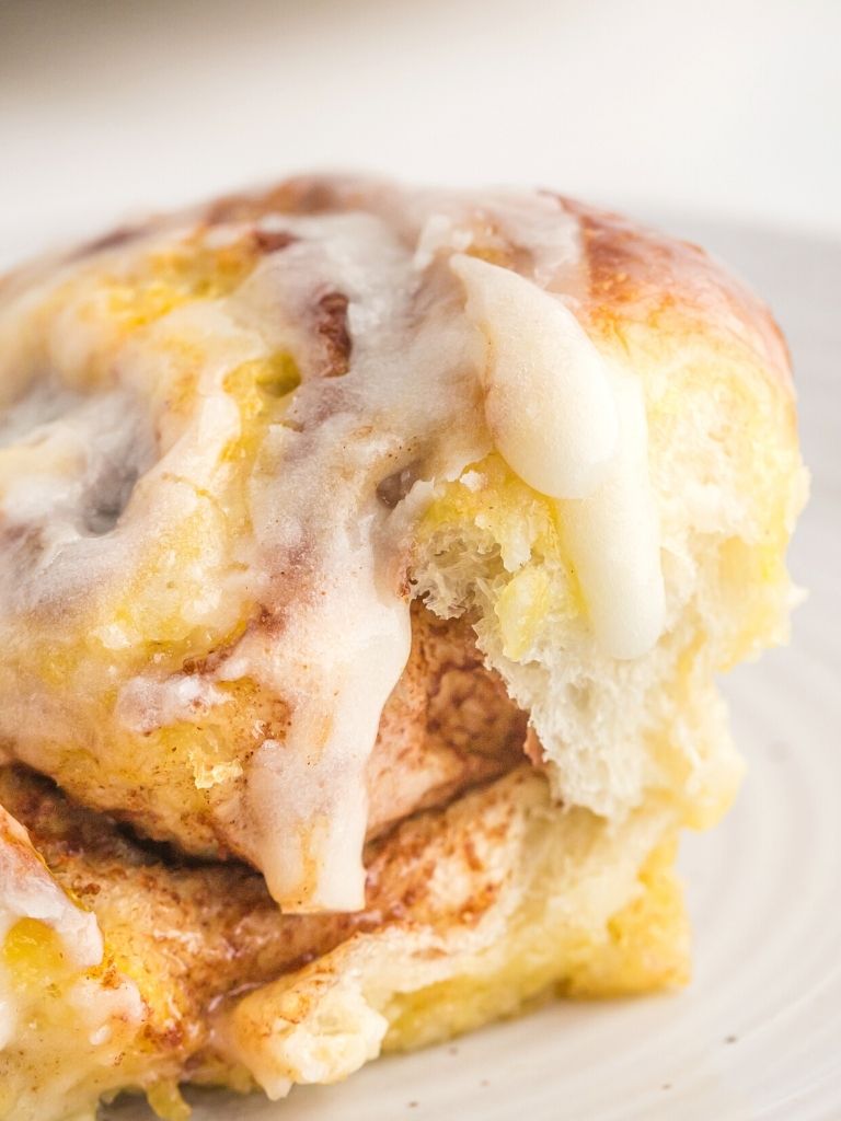 Stack of cinnamon rolls on a white plate with icing drizzling down the side. 