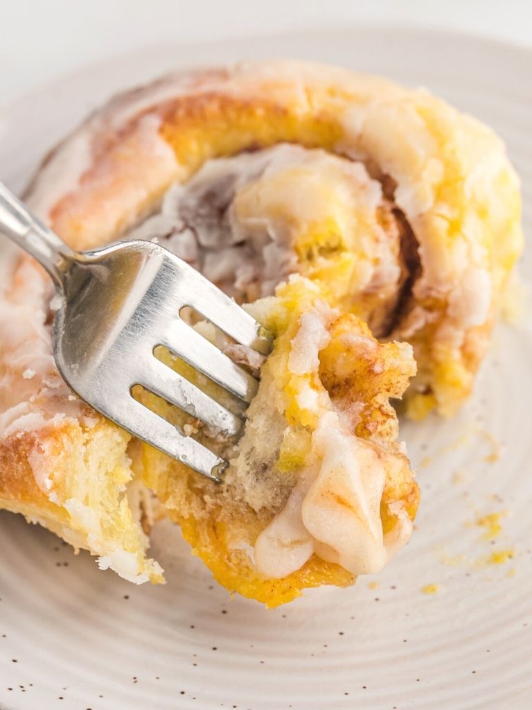 One cinnamon roll on a plate with a fork inside of it. 