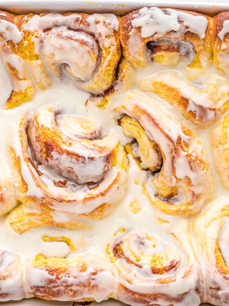 Close up picture of cinnamon rolls with icing inside a white baking dish.