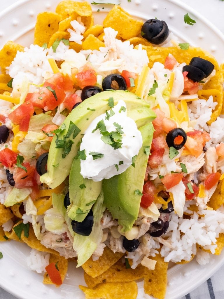 A picture of Fritos chips, topped with rice, and topped with chicken Mexican Haystacks that are made in the slow cooker.