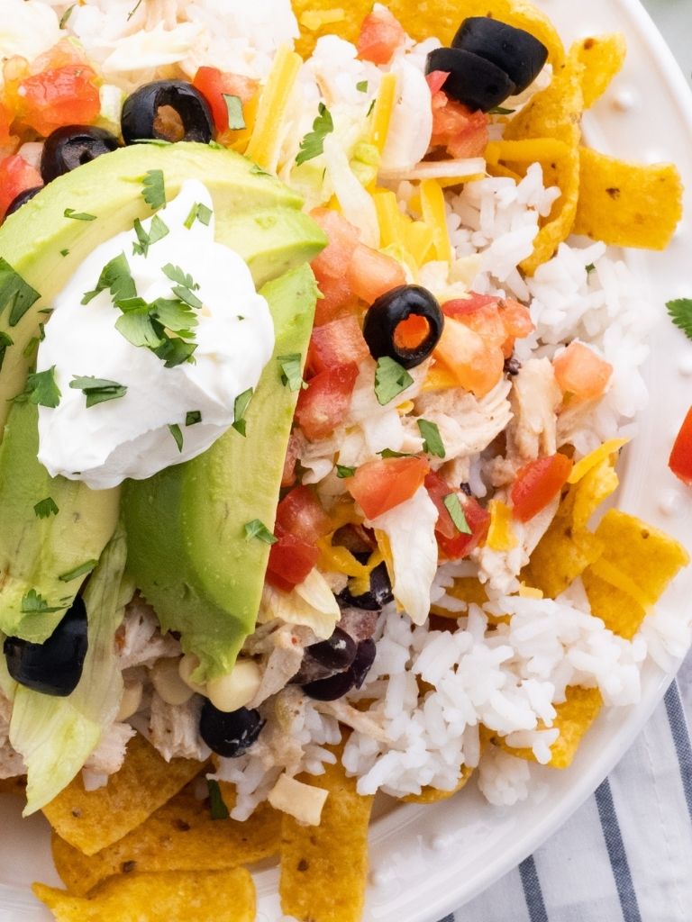 A white plate with rice, corn chips, and Mexican haystack mixture with toppings. 