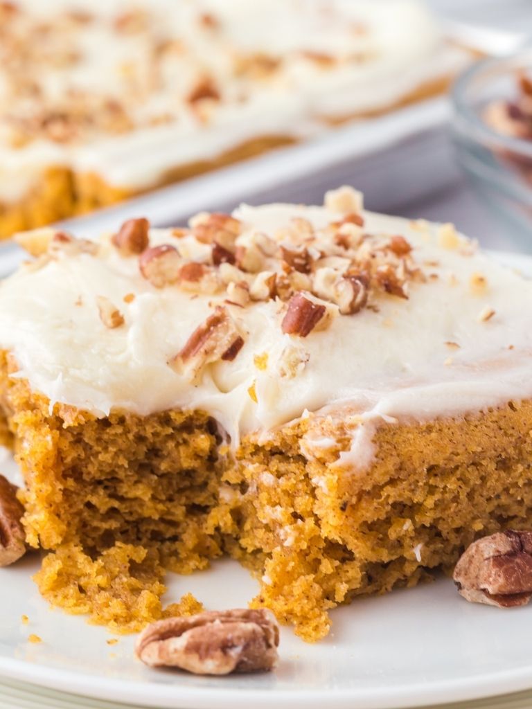 Close up shot of pumpkin spice sheet cake on a white plate and garnished with pecans.