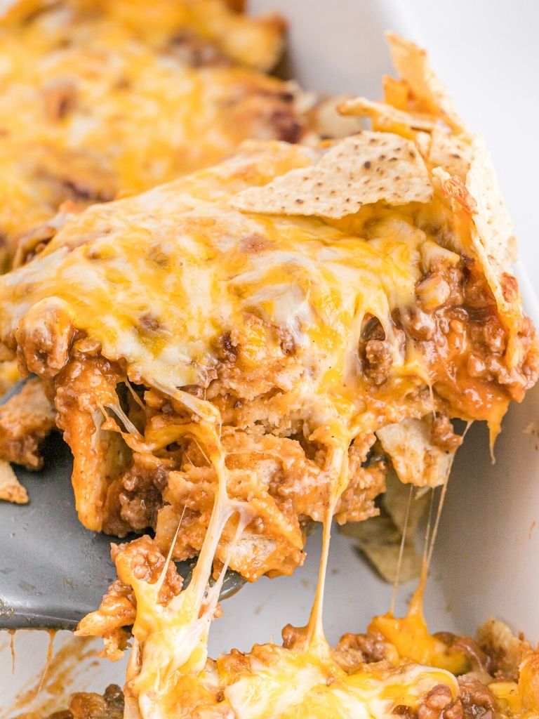 Wooden spoon of casserole with cheese strings hanging down.