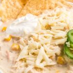 A close up shot of white chicken chili that's so creamy and topped with jalapeño slices, sour cream, chips, and shredded cheese.