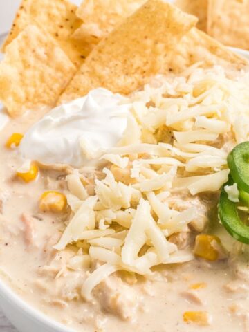 A close up shot of white chicken chili that's so creamy and topped with jalapeño slices, sour cream, chips, and shredded cheese.