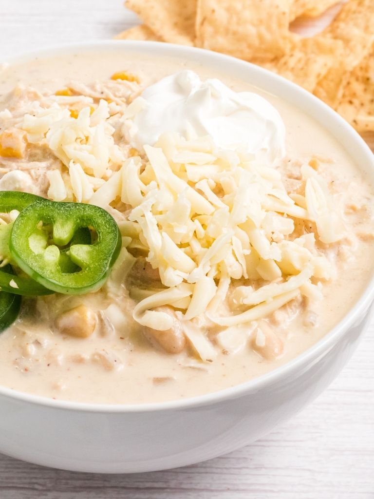 A white bowl with chicken chili inside of it topped with sour cream and jalapeño slices for garnish.