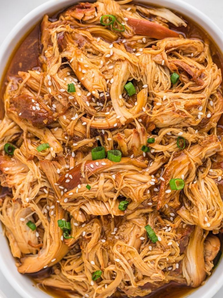 a white dish full of shredded teriyaki chicken with honey. Garnished with green onions and sesame seeds.