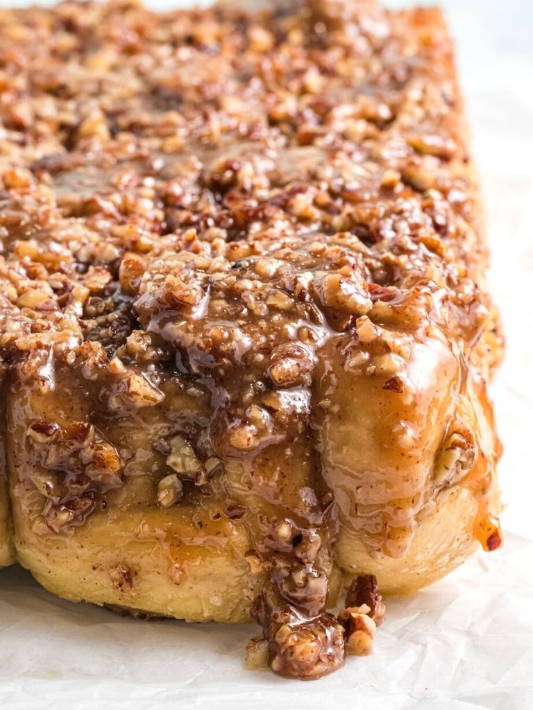 Close up shot of Carmel cinnamon rolls with pecan topping on a white background. 