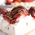 A slice of cheesecake cream pie topped with strawberries and chocolate drizzle.