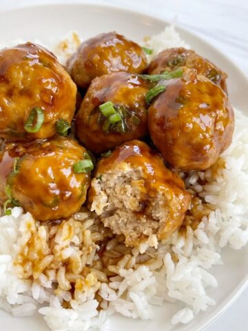 A plate with white rice on it and ground chicken pineapple teriyaki meatballs garnished with green onion.