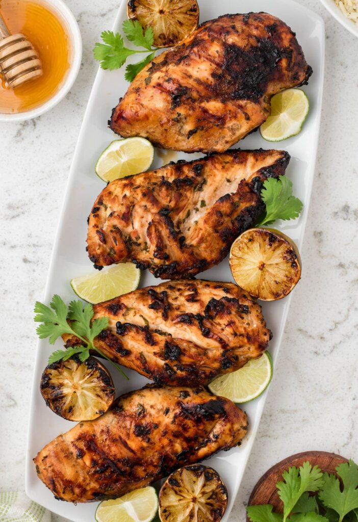 Tray of grilled chicken with a bowl of honey beside it. 