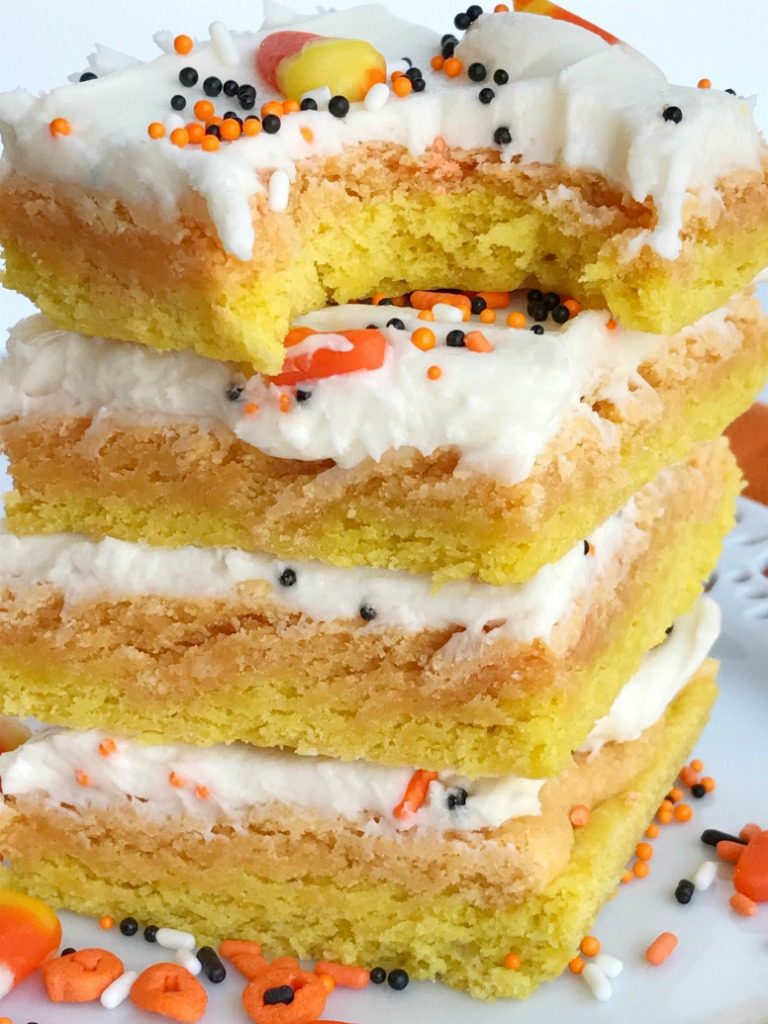 Candy corn sugar cookie bars are the best way to celebrate Halloween. Sugar cookie bars made in a sheet pan so there is plenty for everyone. Layered in yellow & orange sugar cookies and then topped with a white cream cheese icing and decorated with candy corn and Halloween sprinkles! These are so addictive and will be the hit of any party. 