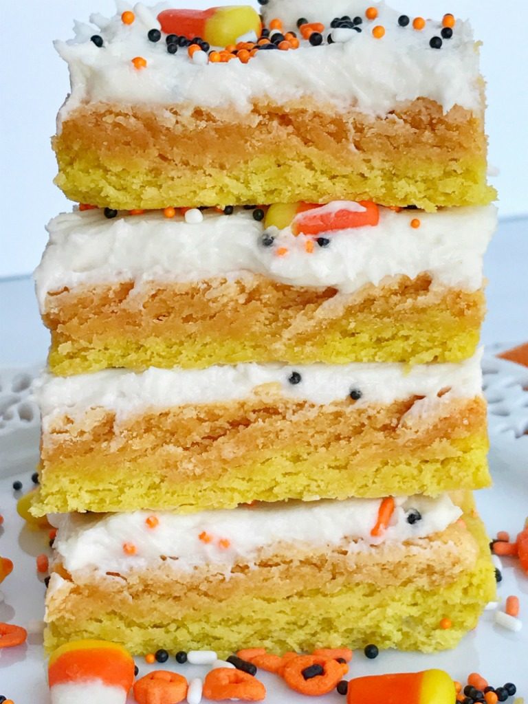 Candy corn sugar cookie bars are the best way to celebrate Halloween. Sugar cookie bars made in a sheet pan so there is plenty for everyone. Layered in yellow & orange sugar cookies and then topped with a white cream cheese icing and decorated with candy corn and Halloween sprinkles! These are so addictive and will be the hit of any party. 