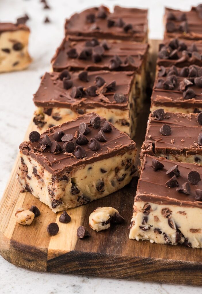 A wooden cutting board with squares of the cookie dough bars on it. 