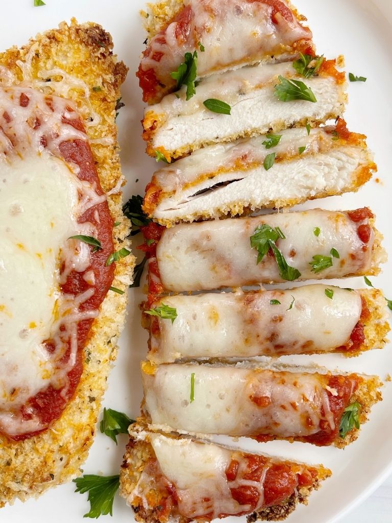 Parmesan chicken cut into slices and topped with cheese and parsley.