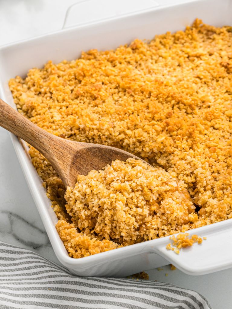 A wooden spoon inside a sweet potato casserole topped with buttery crackers.