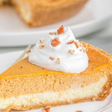 Slice of double layer pumpkin cheesecake on a white plate topped with whipped cream and pecans.