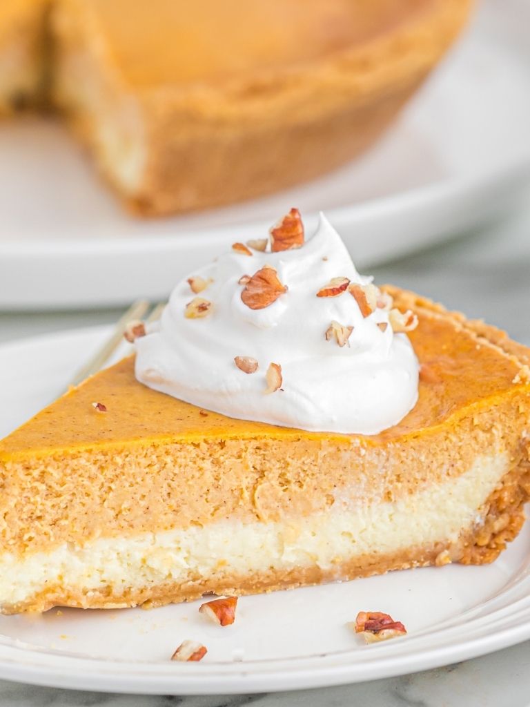 Slice of double layer pumpkin cheesecake on a white plate topped with whipped cream and pecans.