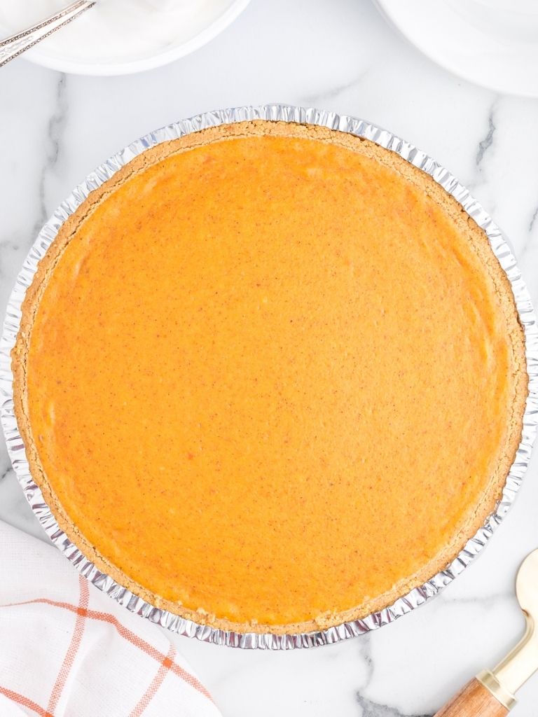 Pumpkin cheesecake in a tin foil crust on a white background.
