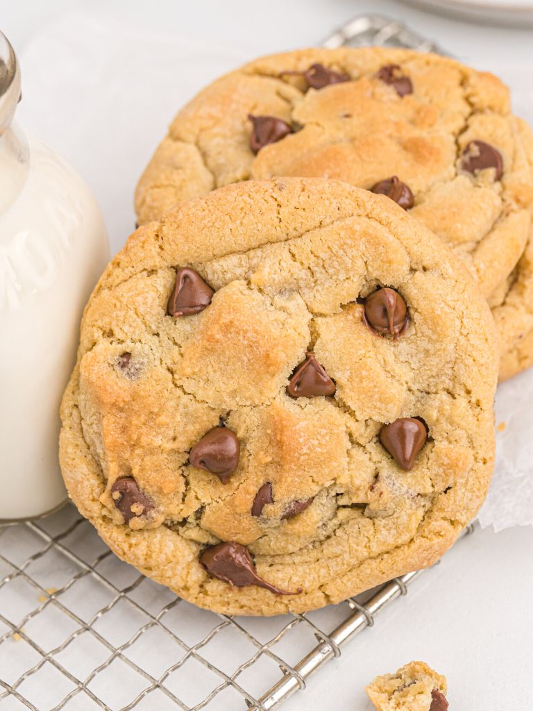 A cookie leaning on a stack of more cookies next to a glass cup of milk.