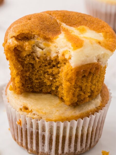 A stack of two muffins with the top one with a bite out of it
