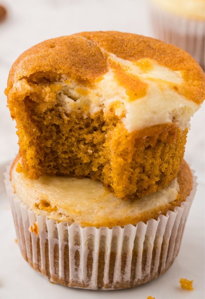 A stack of two muffins with the top one with a bite out of it