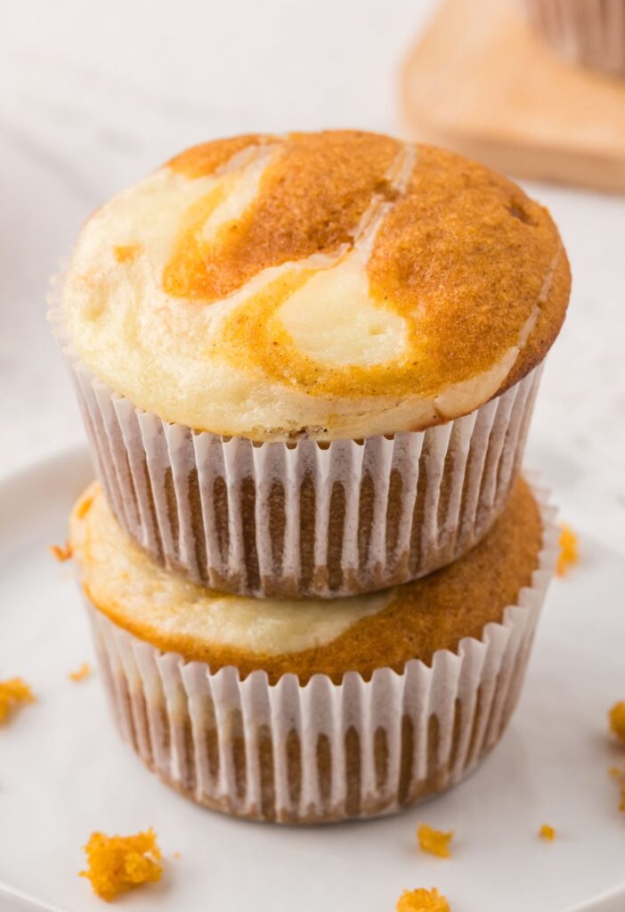 Two pumpkin muffins with a cheesecake swirl stacked on top of each other.