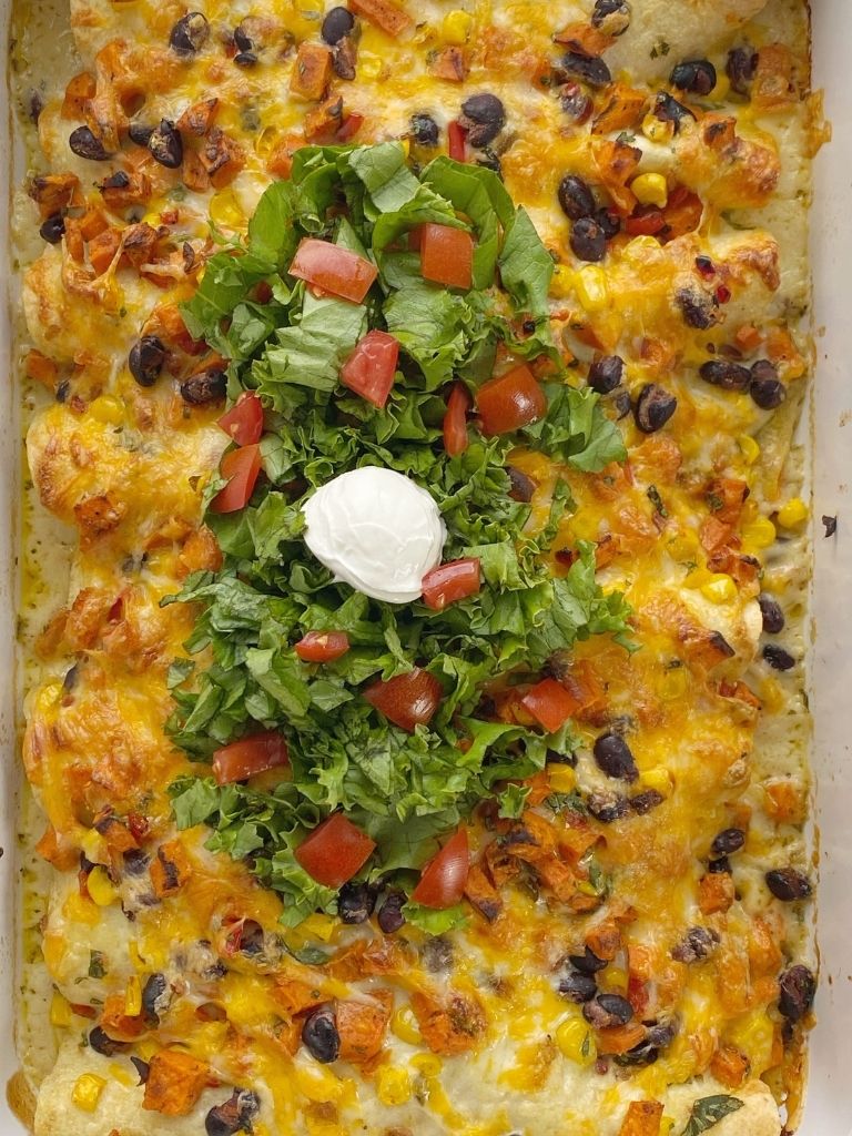 A pan of roasted sweet potato enchiladas topped with green chili enchilada sauce and cheese. 