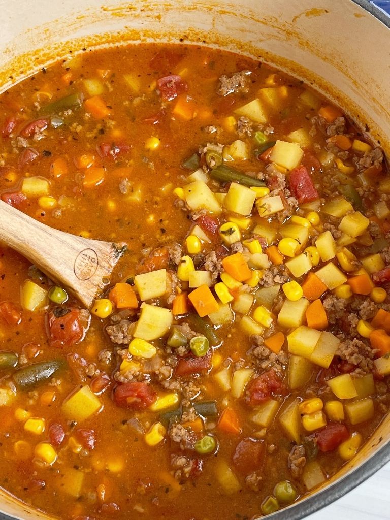 A pot of hamburger soup with a wooden spoon inside it.