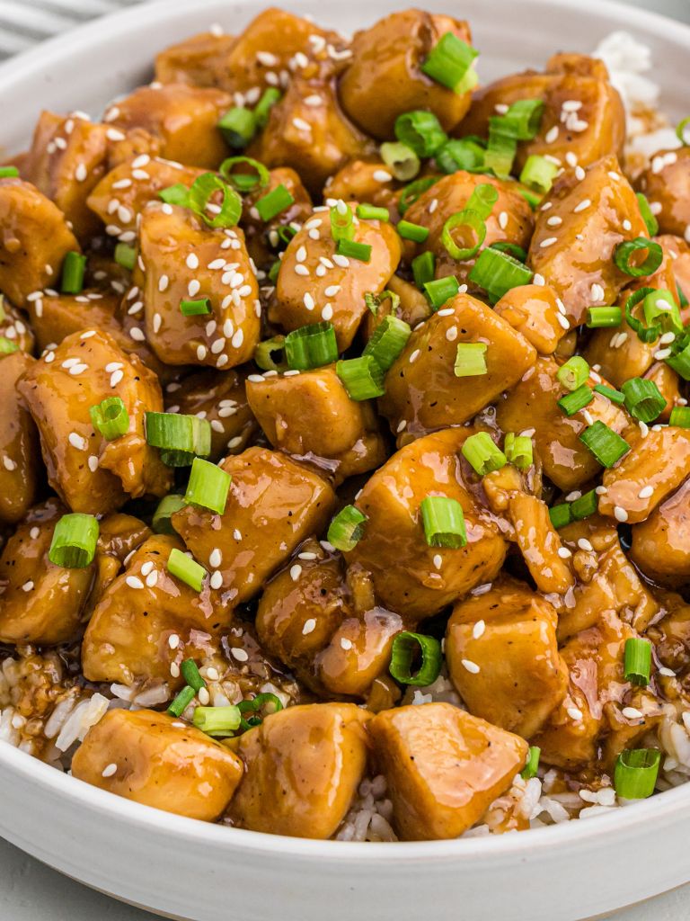 Teriyaki chicken inside a white bowl garnished with green onions.