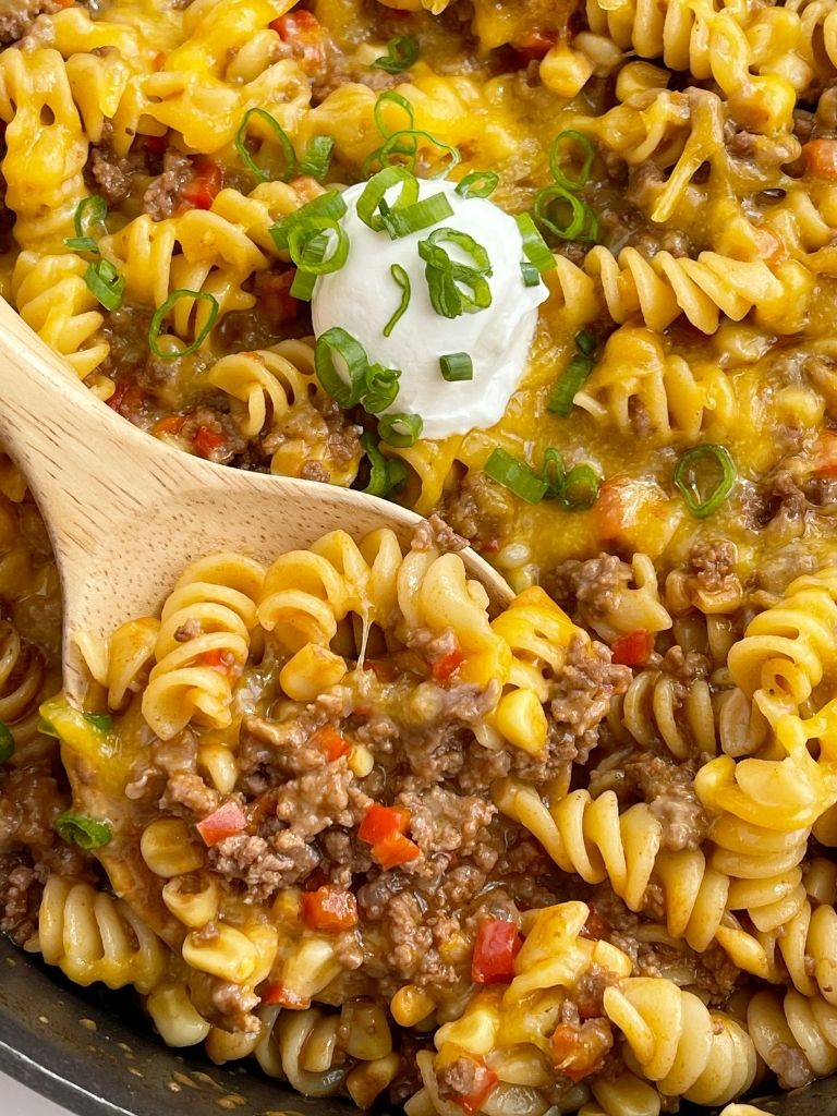 One pan bbq pasta skillet with ground beef shown in a pan with a wooden spoon taking a scoop out of it.